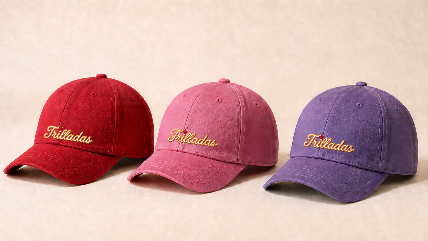 Gorras de Las Trilladas en rojo, rosa y morado con la cereza característica sobre la letra i